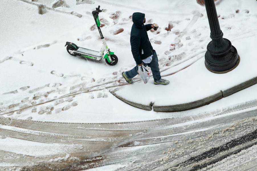 A man walks away from a scooter in that's parked in the snow