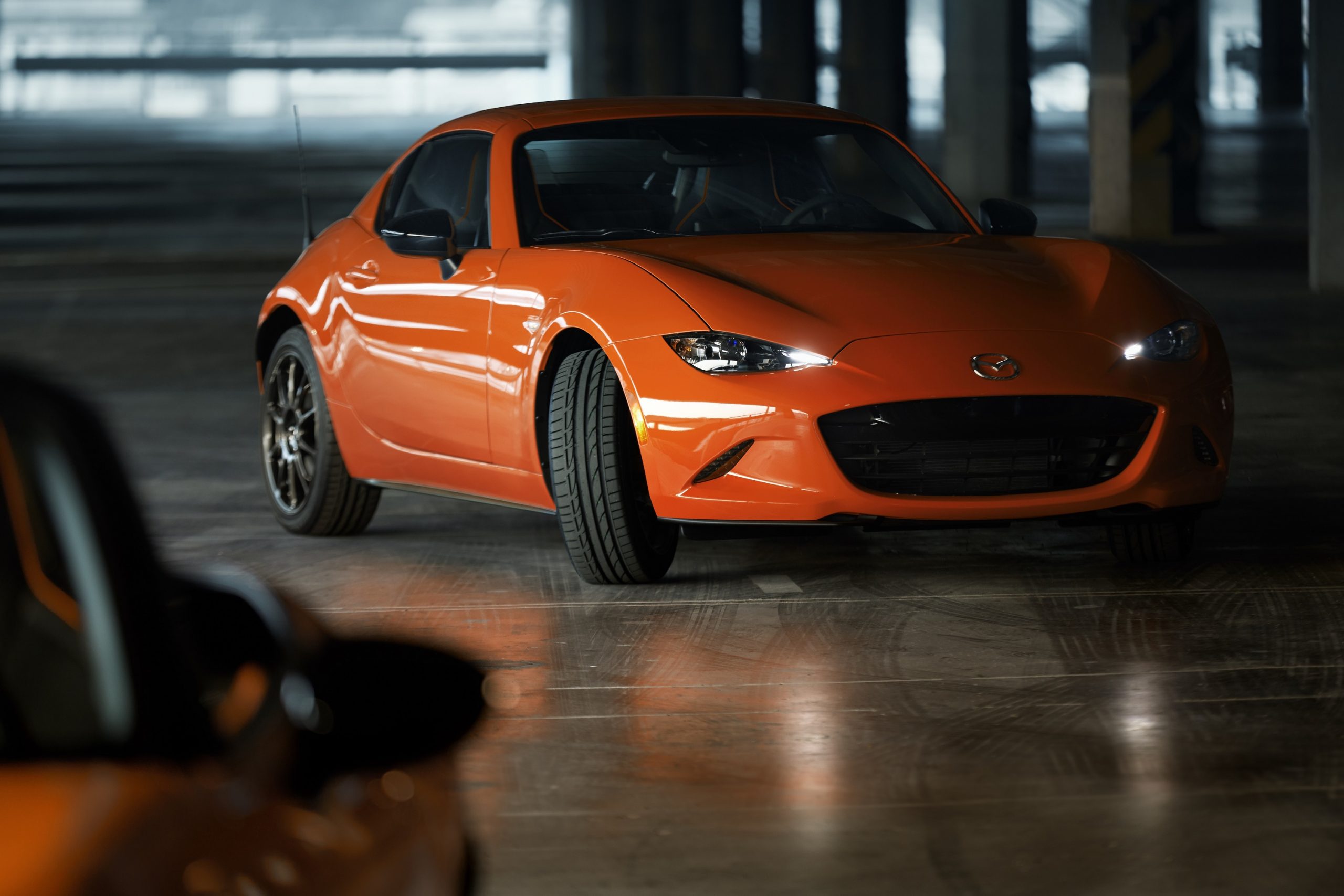 An orange Mazda Miata shot in a shadowy warehouse from the front 3/4