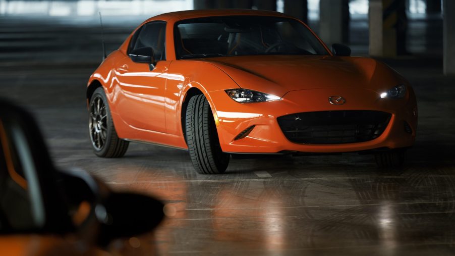 An orange Mazda Miata shot in a shadowy warehouse from the front 3/4. The Mazda Miata is not being discontinued.