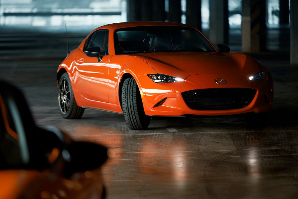 An orange Mazda Miata shot in a shadowy warehouse from the front 3/4. The Mazda Miata is not being discontinued. 