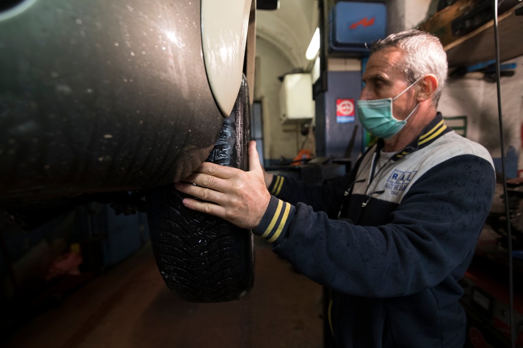 A mechanic inspects a wheel on a car in his shop.