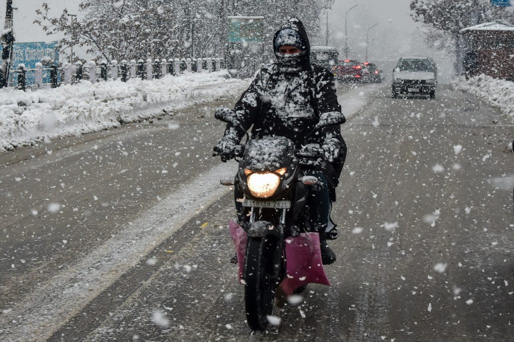 A motorcycle rider rides on a snowy street.