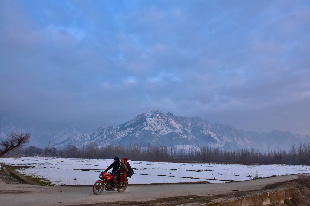 A motorcyclist rides along the road with snow-clad mountains in the backdrop during a winter evening in Srinagar. Weather across the Srinagar city has improved after Kashmir received fresh snowfall