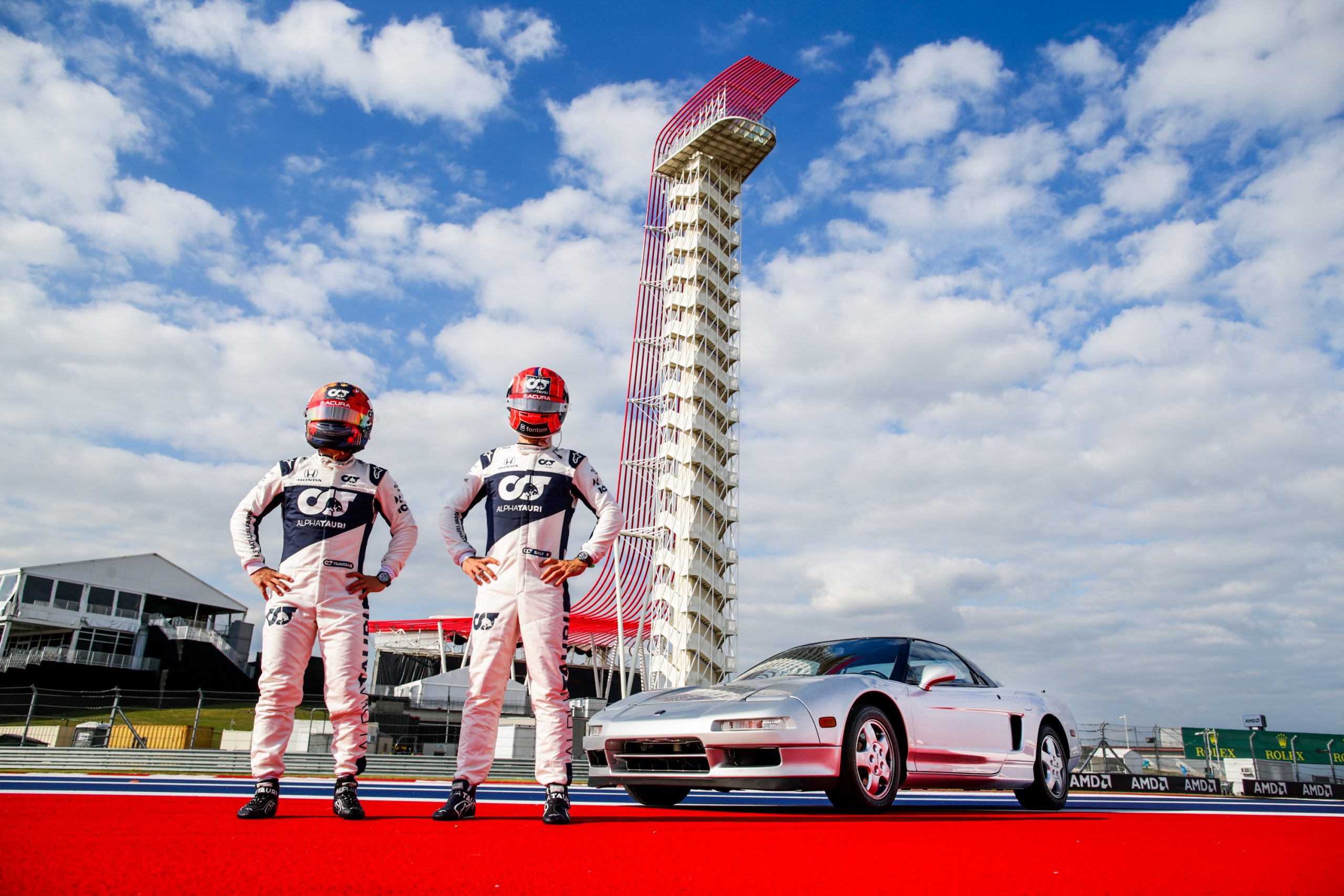 Pierre Gasly and Yuki Tsunoda stand in front of a silver Acura NSX at the Circuit of the Americas
