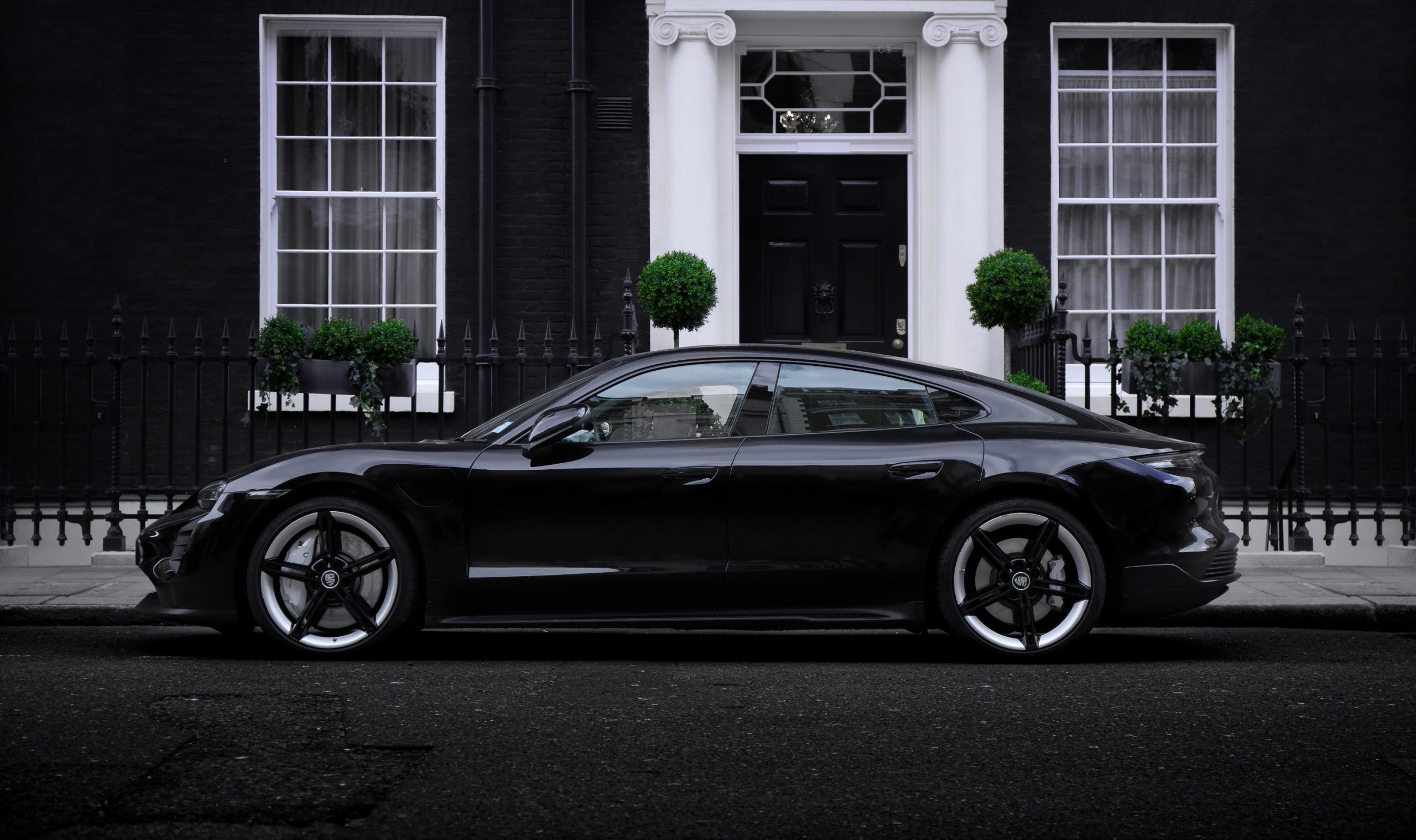 A black Porsche Taycan Turbo S shot in profile while parked on a London curb