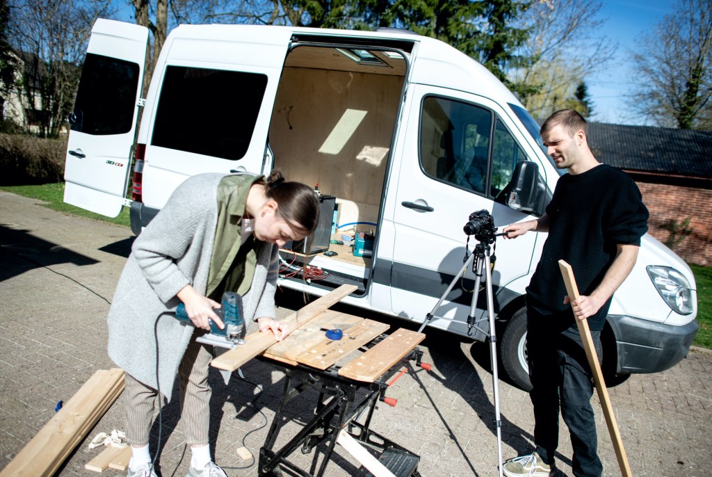 Greta Thomas and Hannes Wehrmann are cutting wood in front of their Mercedes-Benz Sprinter, which the couple is converting into a campervan.