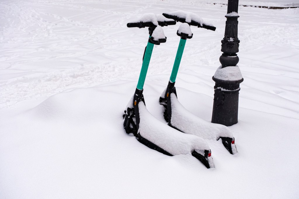 Two electric scooters parked in winter, covered in snow