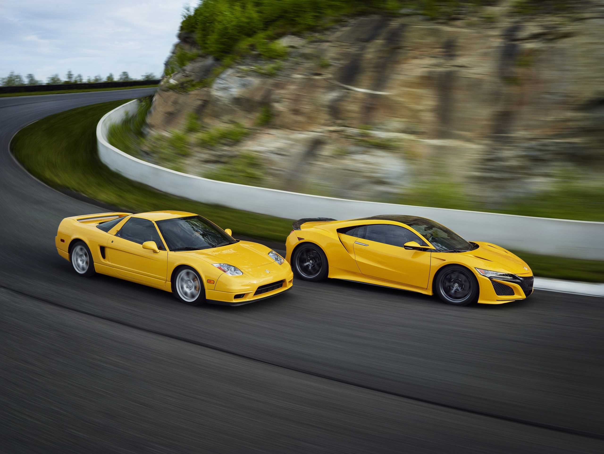 A pair of Spa Yellow Acura NSX sports cars shot in motion from the side