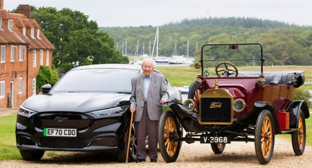 101-year-old Harold Bagott stands beside a Ford Mustang Mach-E  and a Ford Model T.