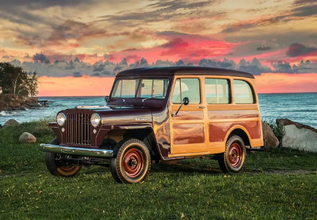 A maroon 1949 Willys-Overland Station Wagon on a grassy hill overlooking the ocean