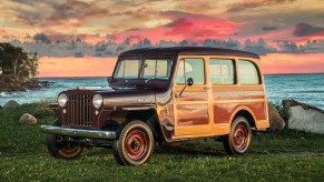 A maroon 1949 Willys-Overland Station Wagon on a grassy hill overlooking the ocean