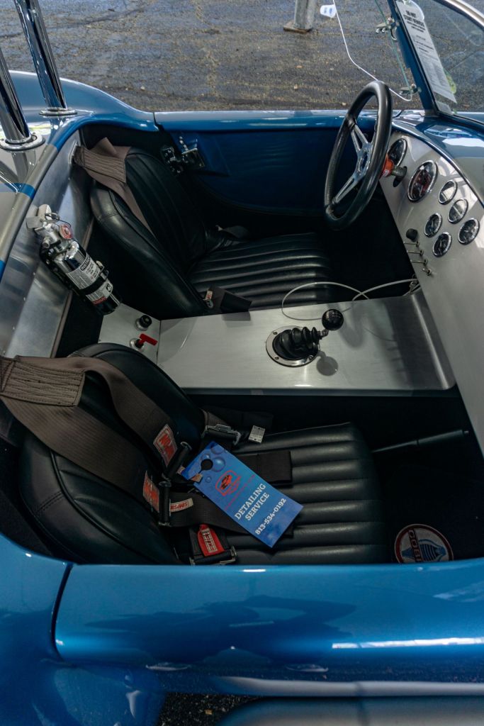 The black-leather-upholstered seats, metal dashboard, and fire extinguisher of a blue-and-silver 1965 Ford Shelby Cobra replica at the 2021 Chicago Mecum auction