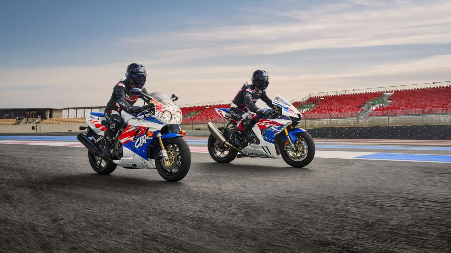 Two black-clad riders on white-red-and-blue 1992 Honda CBR900RR Fireblade next to a 2022 Honda CBR1000RR-R Fireblade SP 30th Anniversary Edition motorcycles