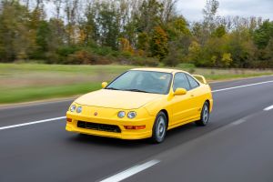 The 2001 Acura Integra Type R compact coupe with a yellow paint color option driving through a stretch of country highway