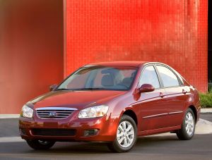 The 2006 Kia Spectra compact sedan in red parked near a red tile wall