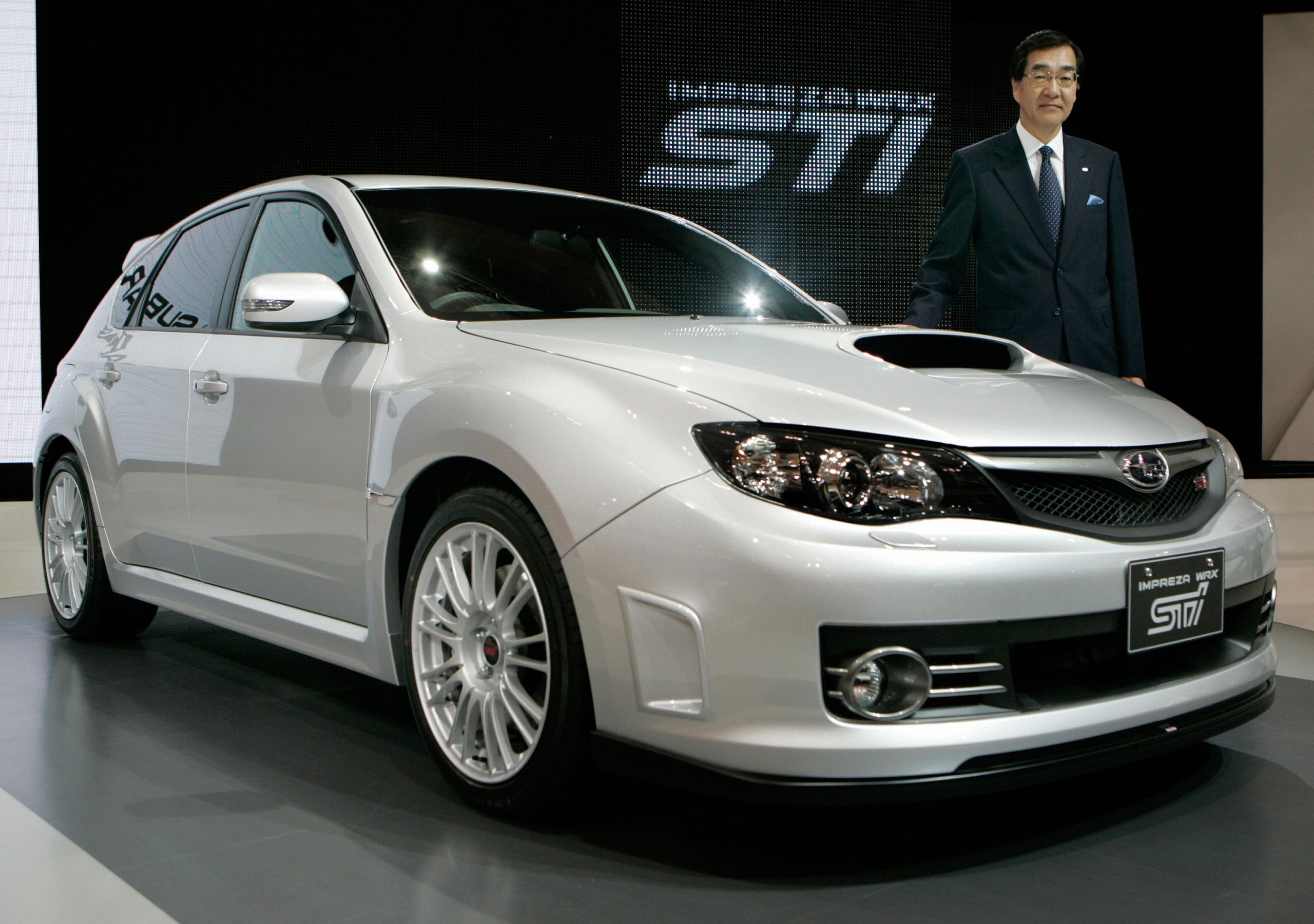 A silver Subaru WRX hatchback on stage accompanied by Ikuo Mori, president of Fuji Heavy Industries