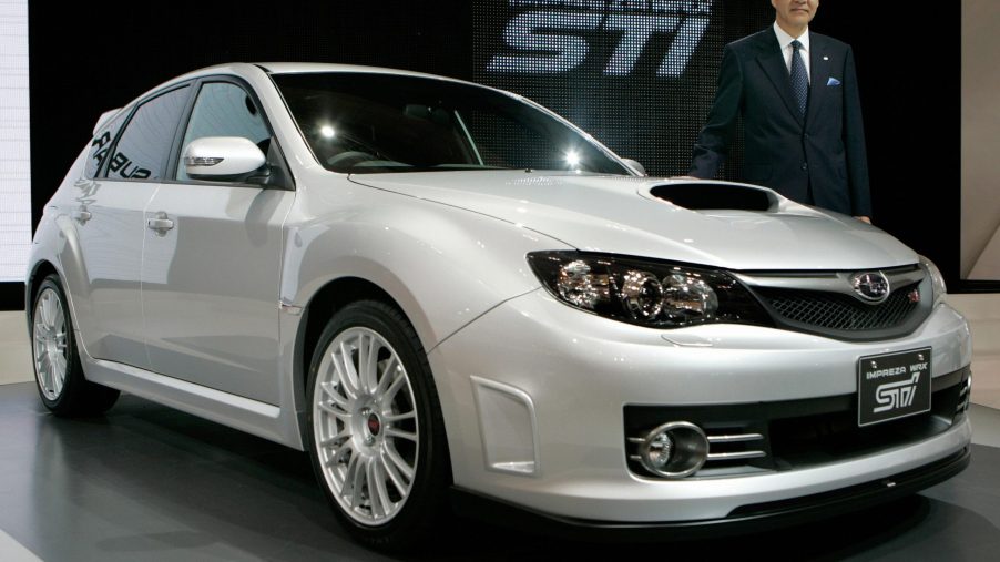A silver Subaru WRX hatchback on stage accompanied by Ikuo Mori, president of Fuji Heavy Industries