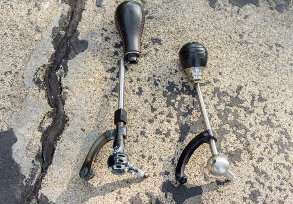 A stock 2013 Fiat 500 Abarth shifter on the ground next to a CravenSpeed short shifter