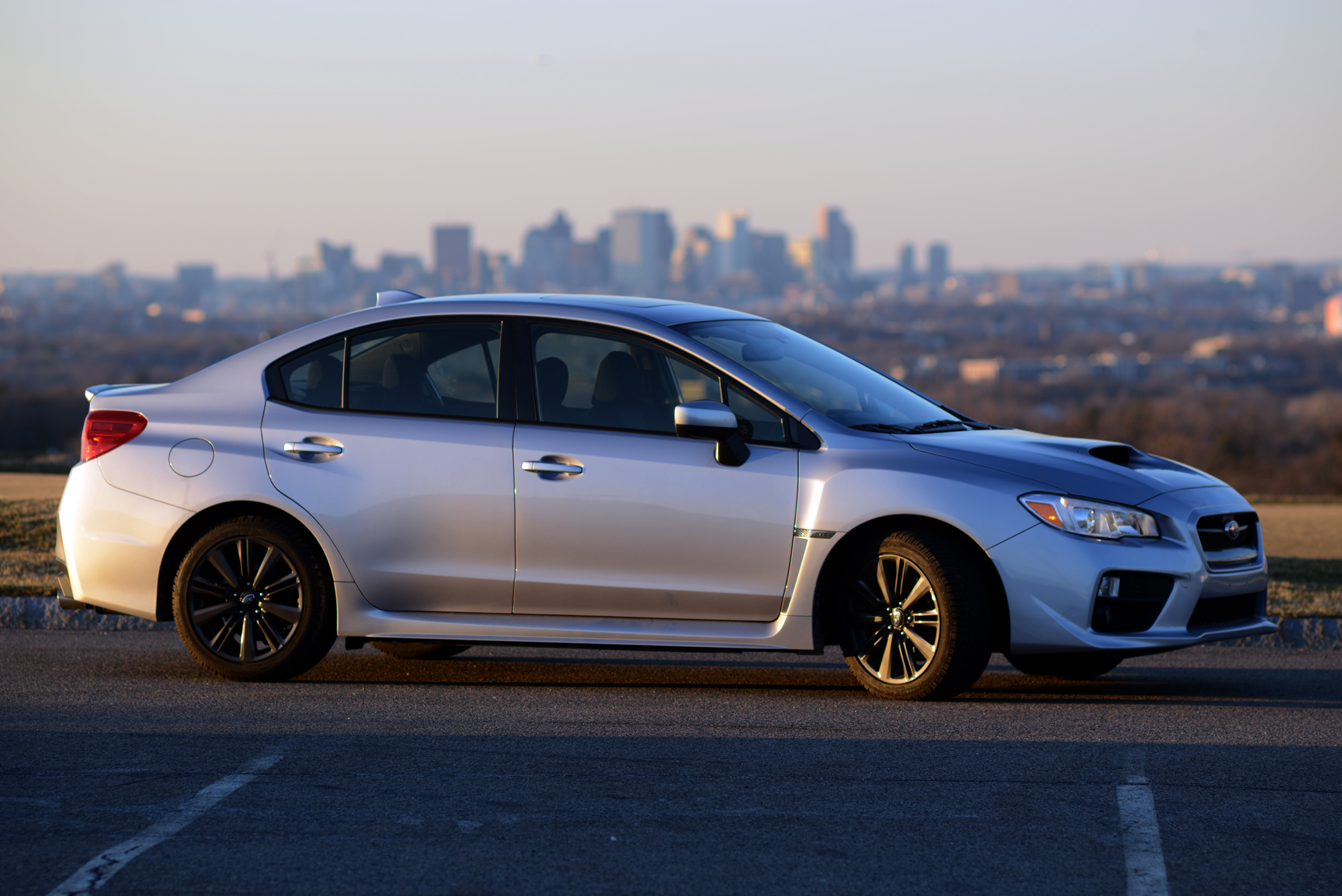 A silver Subaru WRX shot in profile at sunset in a parking lot