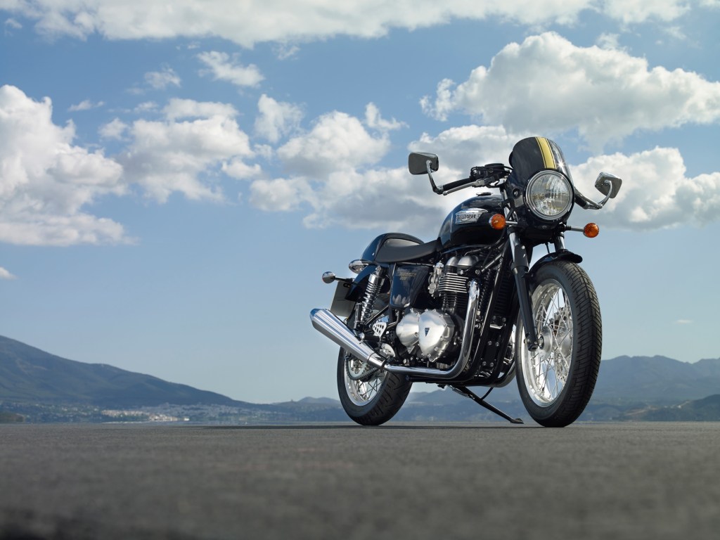 The front 3/4 view of a black-with-gold-stripes 2015 Triumph Thruxton 900 on a runway