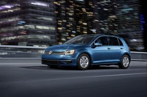 The 2020 Volkswagen Golf compact hatchback in a light blue teal color option driving over a bridge in a city at night