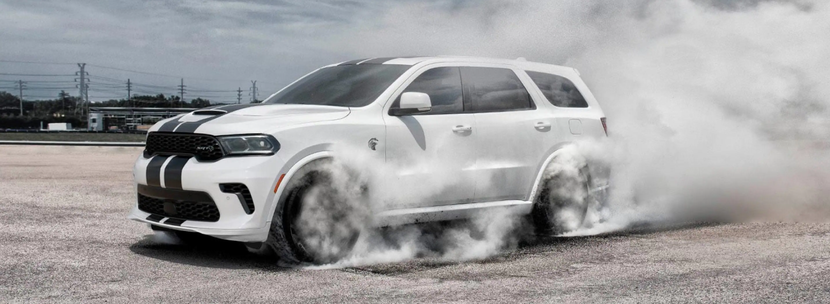 The 2021 Dodge Durango SRT Hellcat muscle three-row SUV in white with a hood vent and stripes as tires spin and generate smoke