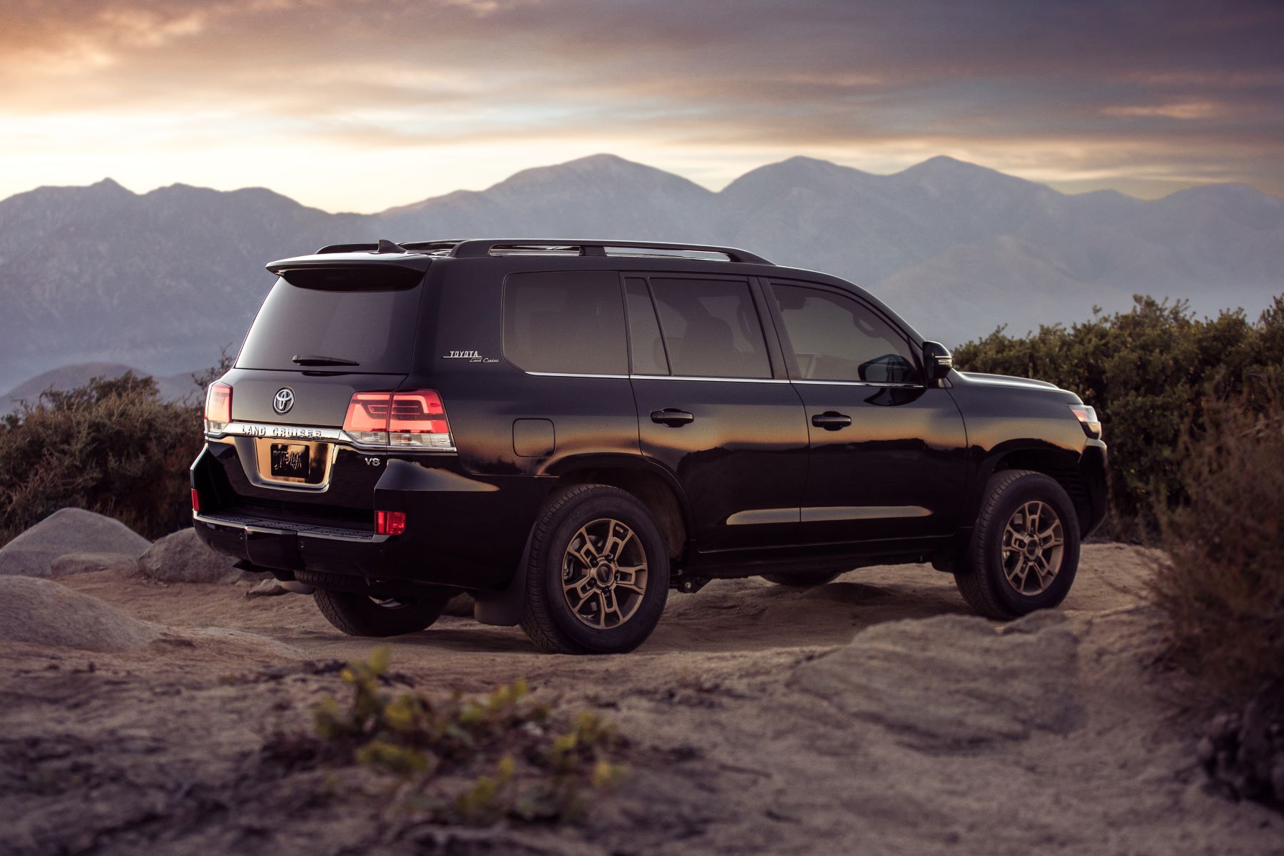 The 2021 Toyota Land Cruiser full-size SUV parked on a rocky mountain cliff in the wilderness at sunset is one of the best luxury SUV models out there.