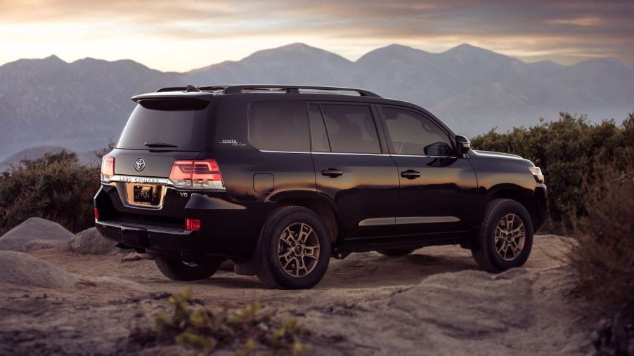 The 2021 Toyota Land Cruiser full-size SUV parked on a rocky mountain cliff in the wilderness at sunset is one of the best luxury SUV models out there.