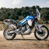 The side view of a blue-white-and-red 2022 Aprilia Tuareg 660 Indaco Tagelmust in the desert