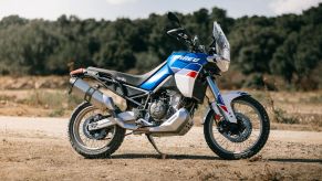 The side view of a blue-white-and-red 2022 Aprilia Tuareg 660 Indaco Tagelmust in the desert
