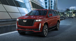 The 2022 Cadillac Escalade luxury full-size SUV with a red paint color option parked outside a building at night near tropical trees