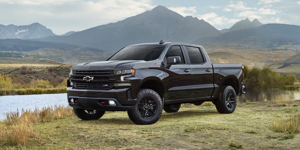 A black 2022 Chevy Silverado parked on grass near a lake with a mountainous background