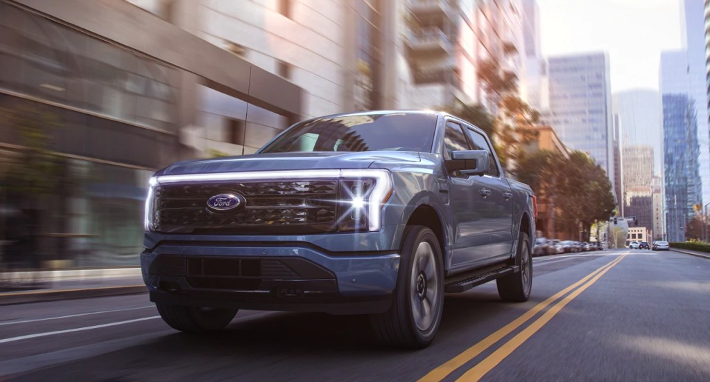 A blue 2022 Ford F-150 Lightning is driving down a city street. 