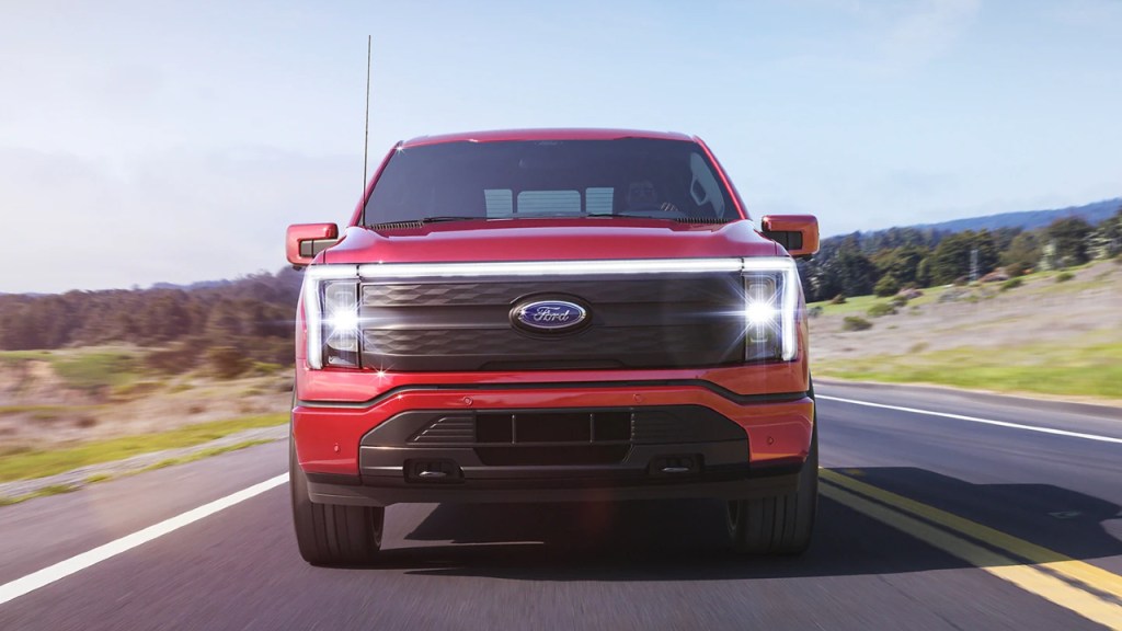 A red 2022 Ford F-150 Lightning is driving down the highway. 