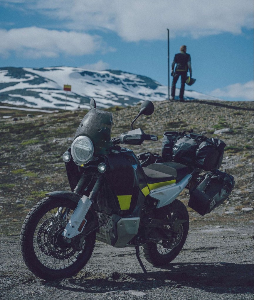 A black-silver-and-green 2022 Husqvarna Norden 901 with accessory bags parked on an alpine country road
