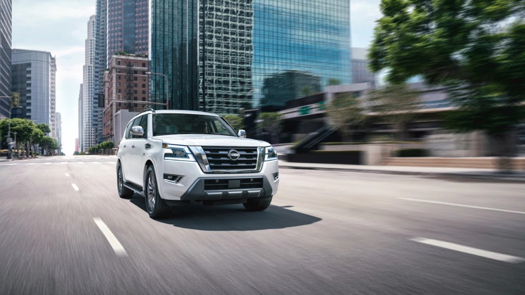 A white 2022 Nissan Armada full-size SUV drives down the road with a city in the background