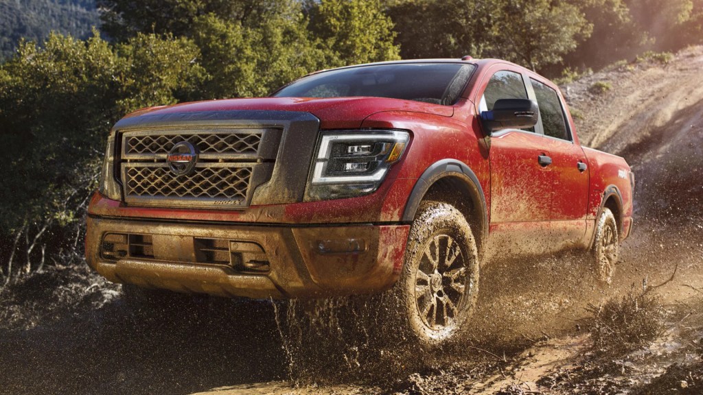 A red nissan titan pro-4x off-road pickup truck drives through mud as it splashes.