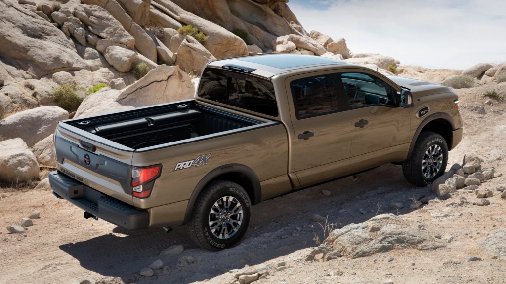 A brown nissan titan pro-4x drives on a dirt road up a hill, an off-road pickup truck.