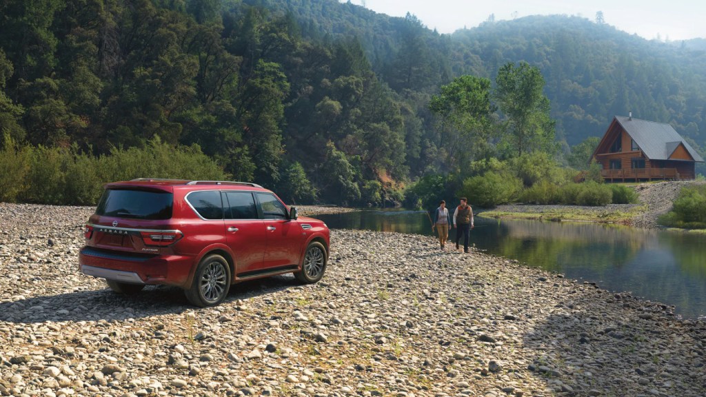A red 2022 Nissan Armada full-size SUV parked near a river with a forest background. How much does a fully loaded one cost?