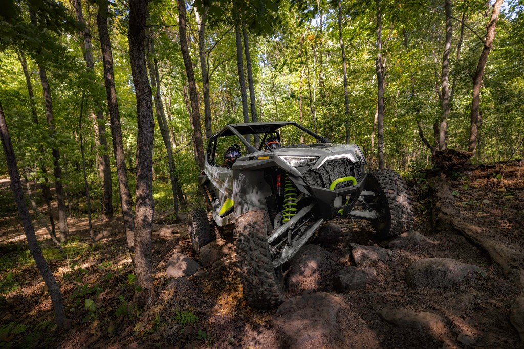 The front 3/4 view of a gray-and-green 2022 Polaris RZR Turbo R Ultimate cresting a hill in the forest