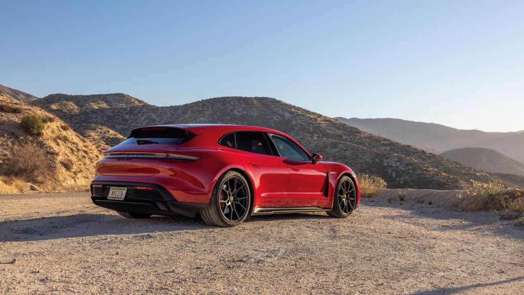 The rear 3/4 view of a red 2022 Porsche Taycan GTS Sport Turismo on a gravel patch overlooking the LA canyons