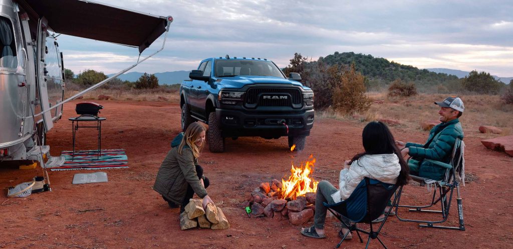 A blue 2022 Ram 2500 heavy-duty pickup truck parked near a group of people camping outdoors.