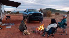 A blue 2022 Ram 2500 heavy-duty pickup truck parked near a group of people camping outdoors.