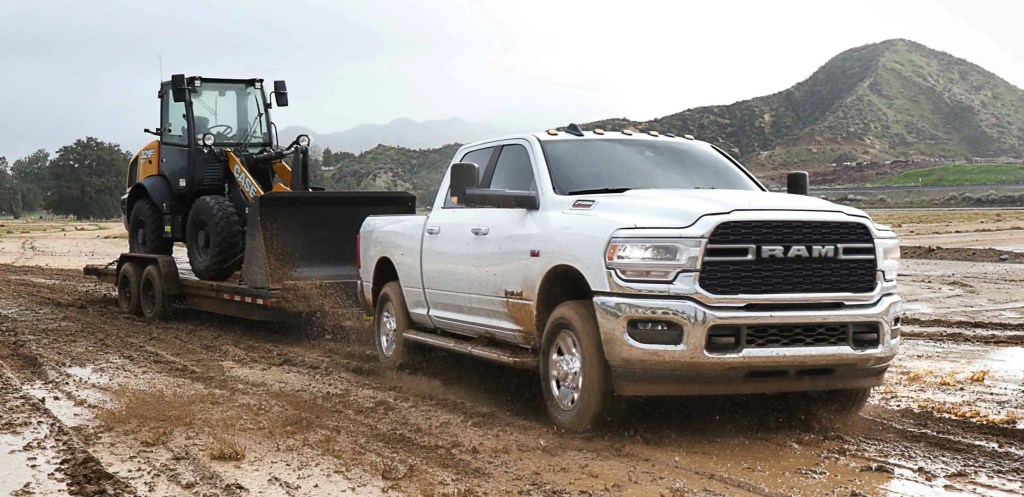 A white 2022 Ram 2500 heavy-duty pickup truck tows a trailer carrying a bulldozer through mud.