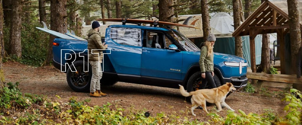 A blue 2022 Rivian R1T with surfboards in the bed and on top. A couple and a golden dog are outside.
