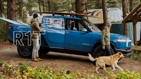 A blue 2022 Rivian R1T with surfboards in the bed and on top. A couple and a golden dog are outside.