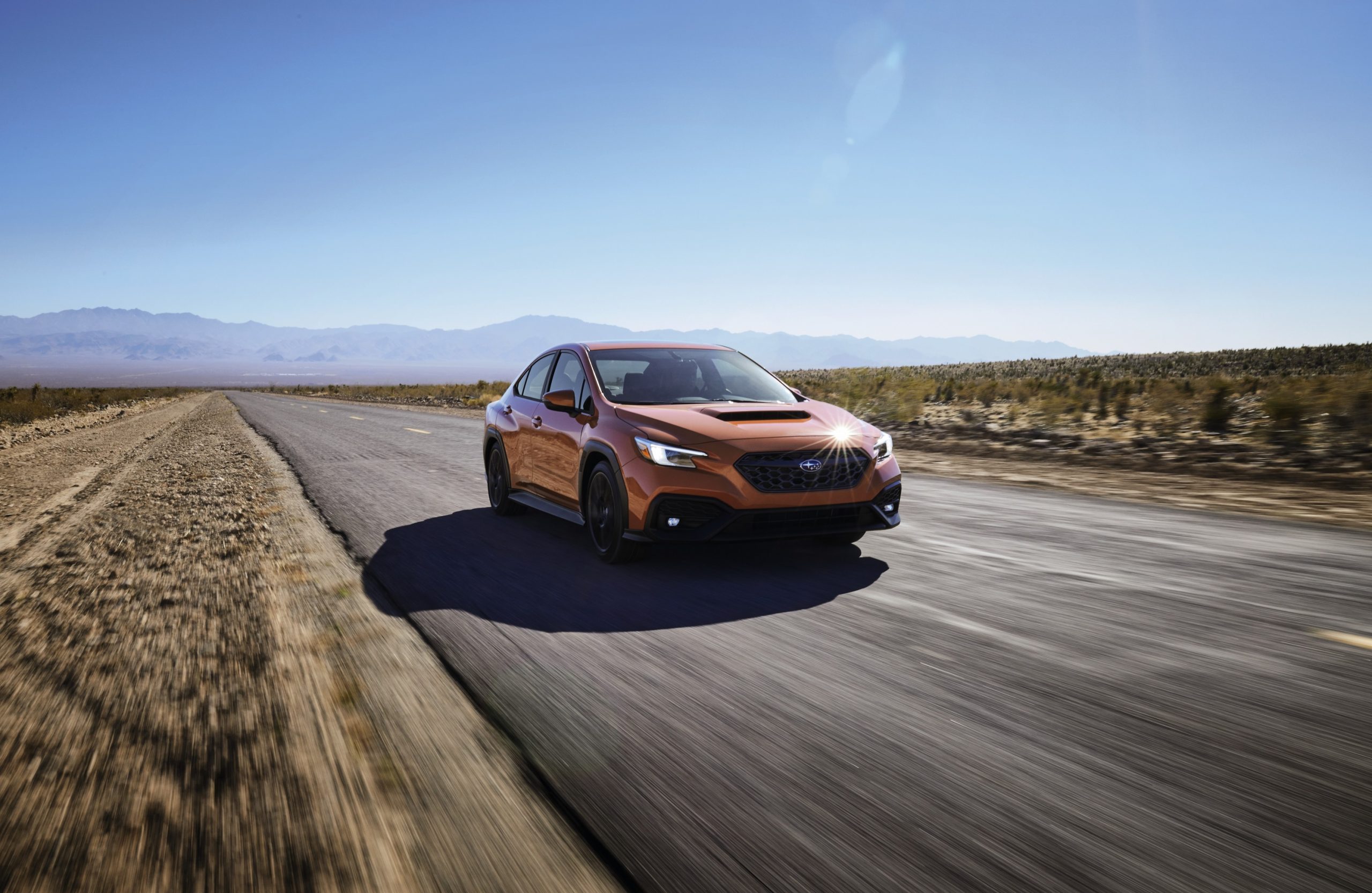 A 2022 Subaru WRX in orange shot blasting down a desert road from the front 3/4