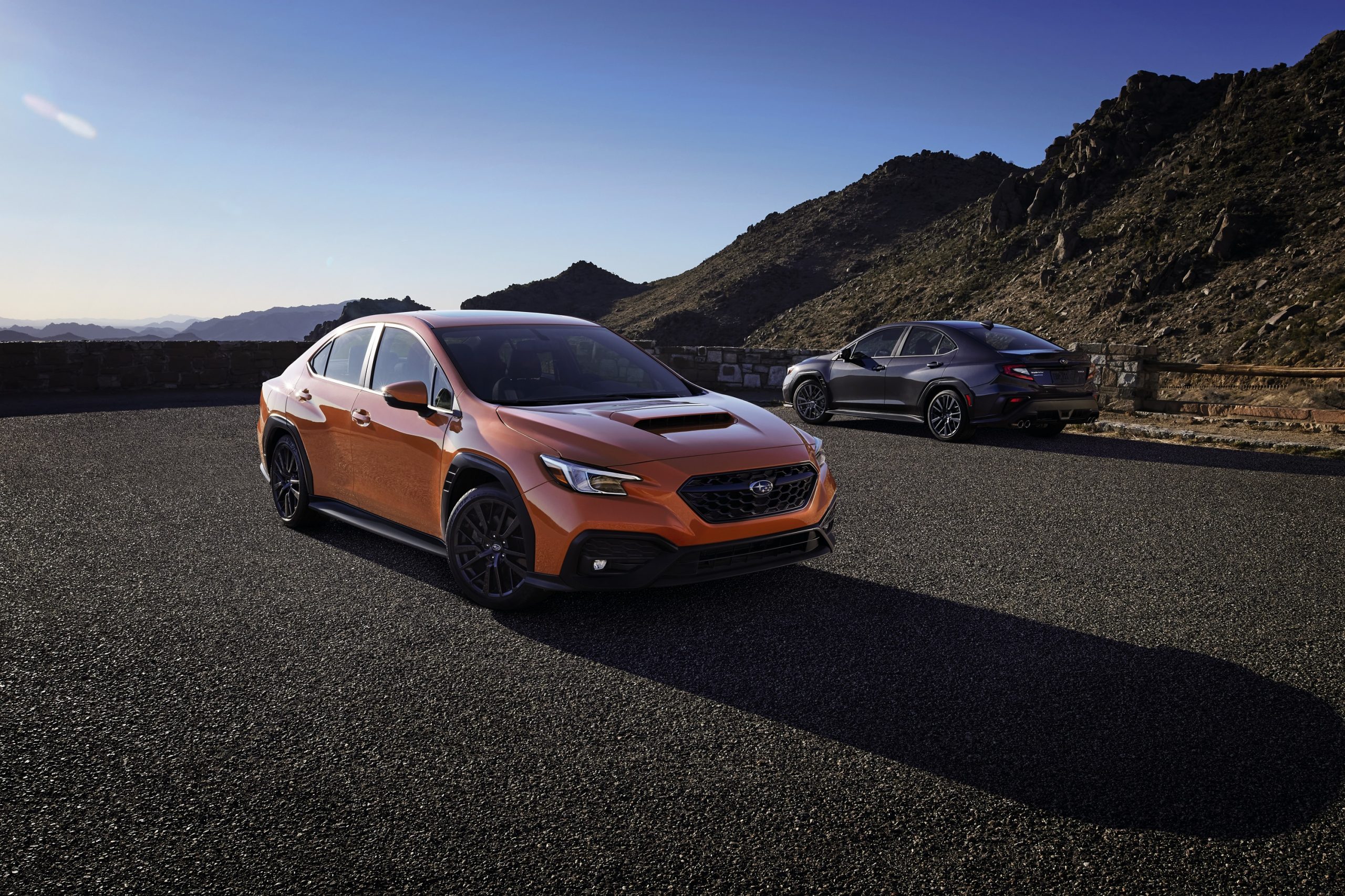 An orange 2022 Subaru WRX shot in the foreground from the 3/4 angle with a blue model behind