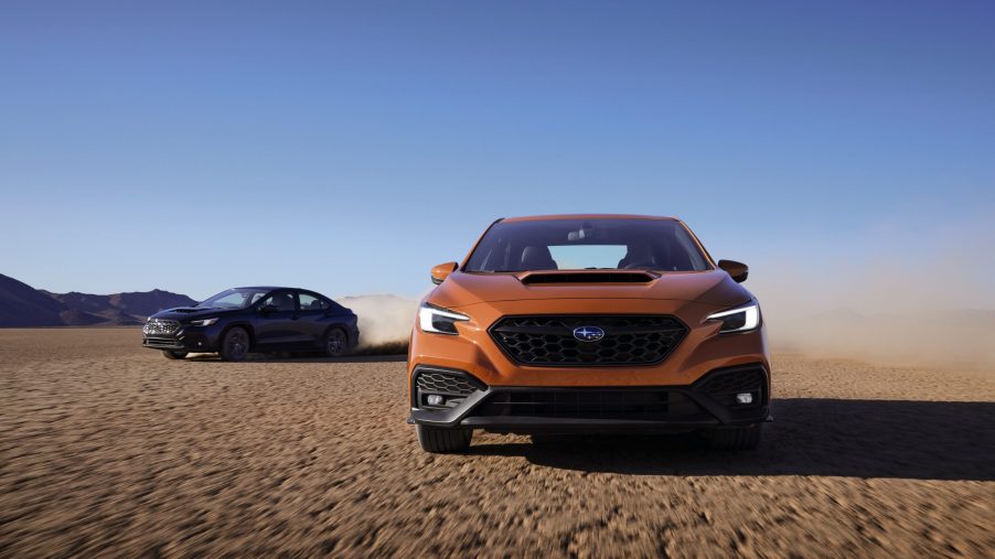 An orange 2022 Subaru WRX shot from the front on a dry lake bed with a blue model close behind