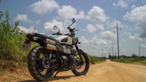 A low-angle rear 3/4 view of a white 2022 Triumph Street Scrambler on a dirt road